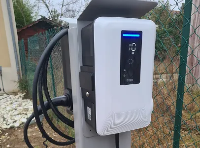 Chargeur de véhicule électrique blanc monté sur poteau, avec câble noir enroulé, près d'une clôture à Vaureal dans le Val d'Oise 95